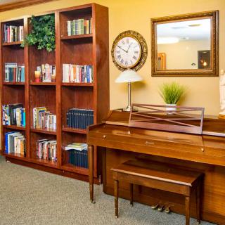 A cozy library corner featuring a wooden bookshelf, a piano, and a decorative clock.
