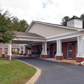 A building with a covered entrance and driveway surrounded by trees.