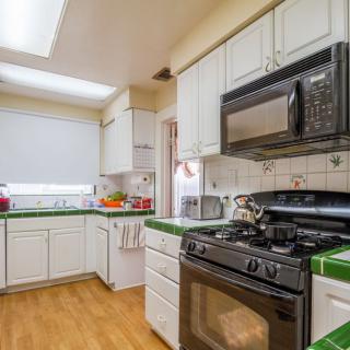 A cozy kitchen featuring a stove, microwave, and white cabinets with green-tiled countertops.