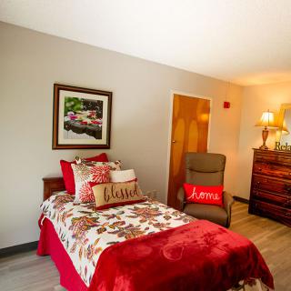 A cozy, well-decorated bedroom featuring a bed with a floral quilt, pillows, and a comfortable armchair.