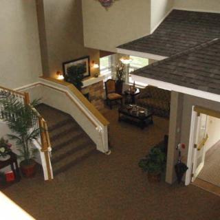 A spacious lobby with carpeted floors, featuring a staircase, potted plants, and a seating area.