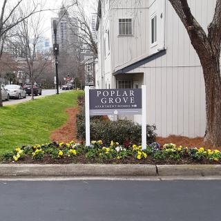 An apartment complex sign surrounded by colorful flowers in an urban setting.