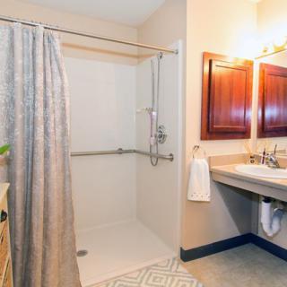 A clean, accessible bathroom with a shower area featuring a handrail, a curtain, and a wide sink with towels.