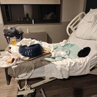 A hospital room showing a cluttered patient bed with leftover food and trash.