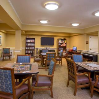 A cozy lounge room with multiple tables and chairs, surrounded by bookshelves and a television on the wall.