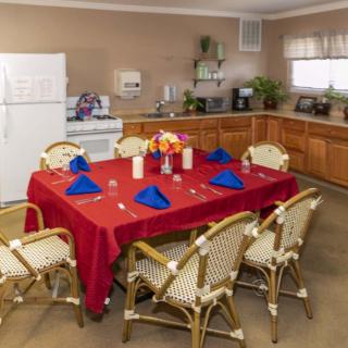 A dining area with a red tablecloth and blue napkins, set for a meal in an adjacent kitchen.