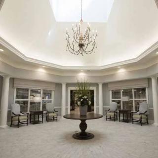 A modern lobby area with a central round table, elegant chandelier, and large skylight.