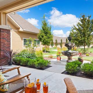 A sunny patio with seating and a picturesque garden featuring a fountain.