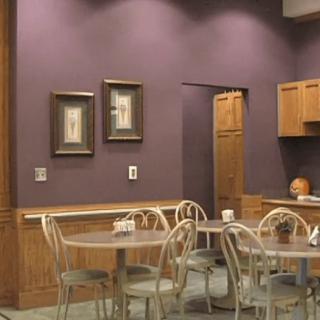 A cozy cafe interior with purple walls, featuring tables and chairs, and framed art on the wall.