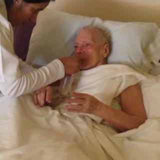 A caregiver assists an elderly person in a hospital bed.