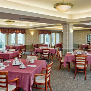 A spacious dining room set up for a meal, featuring neatly arranged tables with red tablecloths and elegant decor.