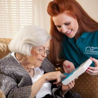 A caregiver assists an elderly woman with reading at home.