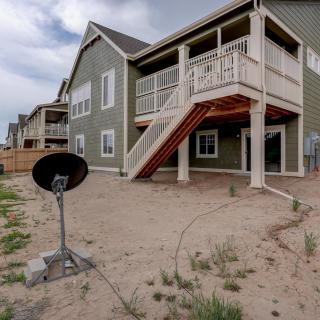 A modern house with a wooden staircase leading to the backyard and a satellite dish on the ground.