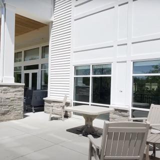An outdoor patio area with chairs and a table in front of a building with large windows.