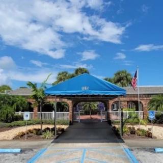 A building entrance with a blue awning, surrounded by palm trees under a clear sky.