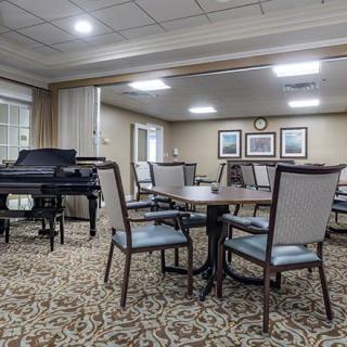 A well-lit dining area with tables and chairs, featuring a piano and framed artwork on the walls.