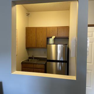 A compact apartment kitchen with a stainless steel refrigerator and wooden cabinets.