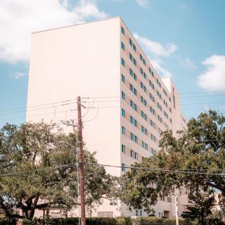 A tall apartment building surrounded by trees under a partly cloudy sky.
