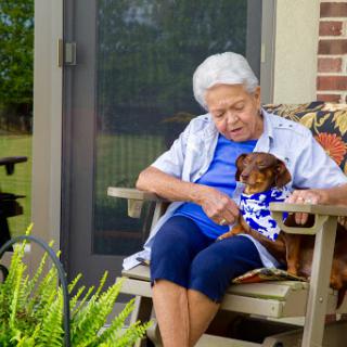 An elderly woman enjoying a peaceful moment on her porch with her dog.