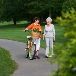 Two women enjoying a walk in the park, with one pushing a bicycle filled with flowers.