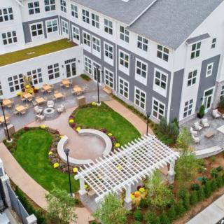 Aerial view of a well-landscaped courtyard with seating areas and a pergola in front of a modern building.