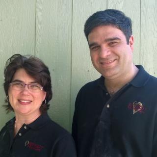 Two people smiling, wearing black shirts, standing outside.