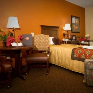 A cozy hotel room with a bed, chairs, and warm decor.