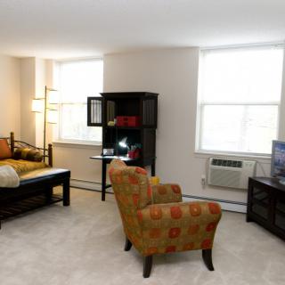 A cozy living room with a sofa, patterned chair, bookshelf, and television.