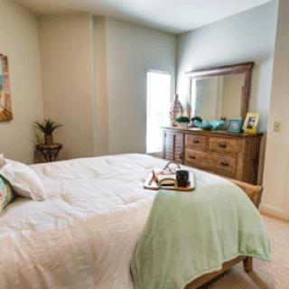 A cozy and well-decorated bedroom featuring a comfortable bed with a light green throw and a wooden dresser with a mirror.