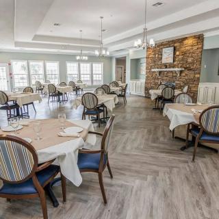 An elegant dining room with neatly arranged tables and chairs, featuring a fireplace and large windows.