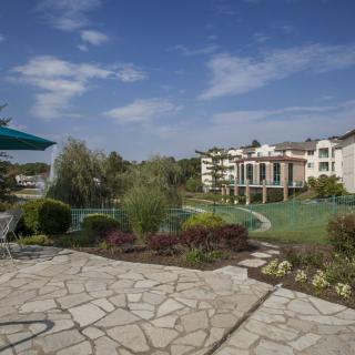 A scenic view of a landscaped garden with a stone patio, overlooking modern buildings under a clear blue sky.