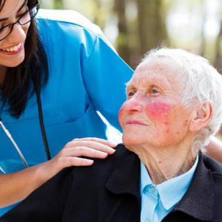 A caregiver providing support to a smiling elderly person outdoors.