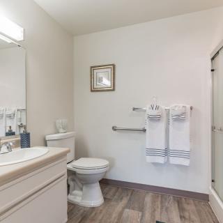 A clean and minimalistic bathroom featuring a toilet, sink with a mirror, shower stall, and neatly hung towels.