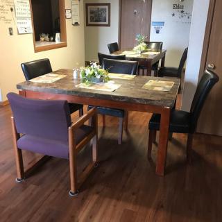 A cozy dining area featuring a wooden table and chairs, with decorative placemats and greenery.