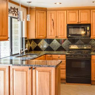 A modern kitchen with wood cabinets, black appliances, and a granite countertop.