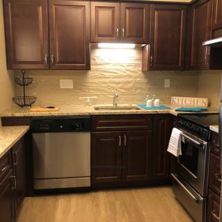 A modern kitchen featuring wooden cabinets, a stove, oven, dishwasher, and a sink with overhead lighting.