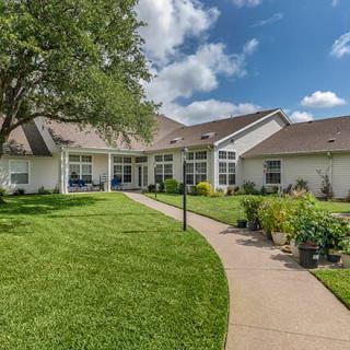 A suburban house with a well-maintained lawn and a garden pathway under a partly cloudy sky.