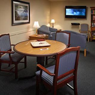 A cozy living room with a round table and upholstered chairs, featuring a television on the wall.