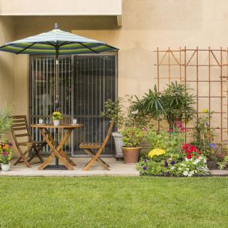 A cozy patio area with a table, chairs, and an umbrella, surrounded by a well-kept garden.
