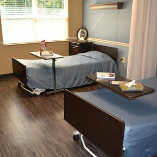 A well-lit hospital patient room featuring two beds with side tables.