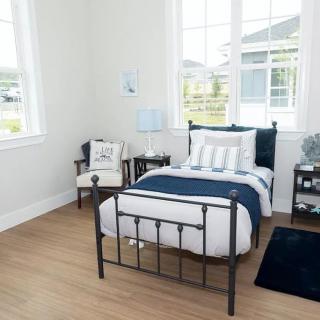 A bright and modern bedroom featuring a single metal-frame bed with decorative pillows, wooden flooring, and large windows.
