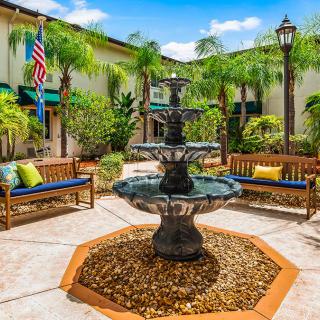 A tranquil courtyard featuring a central fountain surrounded by benches and palm trees.