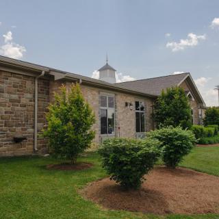 A church building with stone exterior and manicured landscaping under a partly cloudy sky.