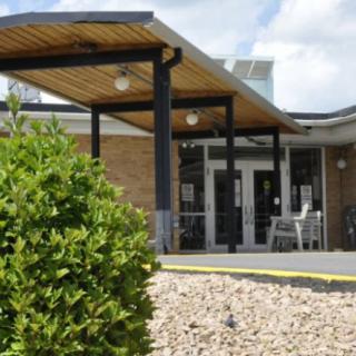 A modern building entrance with a covered walkway and surrounding greenery.