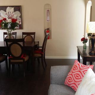 A cozy living and dining area with elegant decor, featuring a dining table, chairs, floral artwork, and a comfortable couch with patterned cushions.
