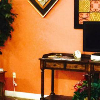 A cozy living room with a wooden desk, art on the walls, and a television against an orange backdrop.