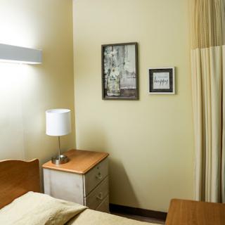A cozy bedroom featuring a lamp, nightstand, and wall art.