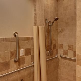 An accessible bathroom with tiled walls, a handheld showerhead, and grab bars.