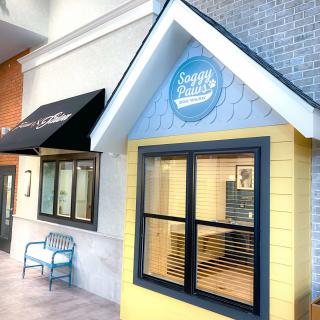 A small storefront with a yellow wall and blue accents, featuring a window, bench, and awning.