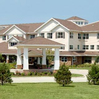 A large residential building surrounded by a manicured lawn and trees.